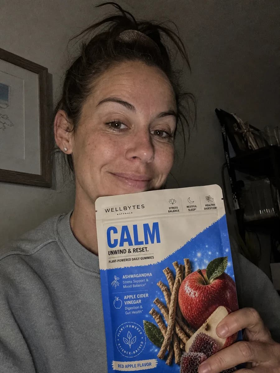 Grainy iPhone-style selfie holding a WellBytes Calm pouch in dim home lighting